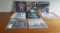 Eight vinyl LP records laid out on floor, mostly in protective sleeves, covers show The Jam and The Clash band images and album titles.