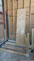 Plywood sheet leaning against the wall and several 2x4 lumber boards placed on the floor and plastic supports.