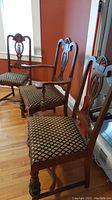 Photo of three wood dining chairs and one armchair with carved backs and upholstered seats in patterned fabric, showing turned legs.