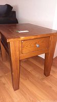 Image of the solid wood end table showing the top, legs, and front drawer with metal pull.