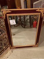 Full view of the antique style beveled mirror with wood frame and gold corner accents against a beige floor with a rug partially visible.