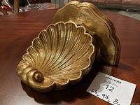 Side angle photo of gold shell wall shelf lying on a table showing profile and backplate.
