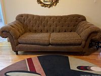 Front view of brown chenille sofa showing tufted back, rolled arms, and two seat cushions on wood floor with area rug in front.
