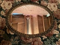 Oval mirror laying on a floral carpet, showing full reflective surface and frame detail.