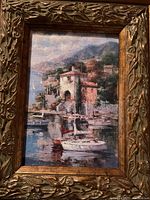 Photo of one of two similar gilt framed paintings depicting coastal landscape with boats and Mediterranean buildings.