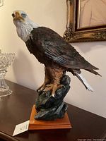 Front-side angle of a large bald eagle sculpture on a rock and wood base, showing detailed feathering and coloring.