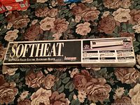 Boxed SofHeat electric baseboard heater on floral carpet, showing front with brand and product type.