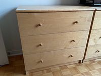 Full front view of the IKEA blonde wood dresser showing the three drawers and their wooden knob handles.