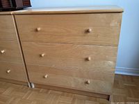 Frontal view of the blonde wood dresser showing three drawers with round wooden knobs.