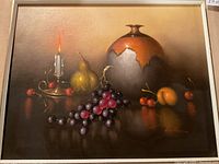 Frontal photo showing the entire still life oil painting featuring the mid-century pottery vase, lit candle, grapes, cherries, apricots, and pear on reflective surface.