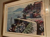 Close-up view of the colorful framed seaside resort print showing flowers, stone wall, and water with boats.