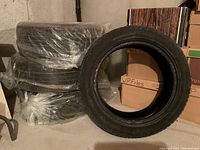 Four car tires stacked on the floor, one tire standing upright showing tread and sidewall details.