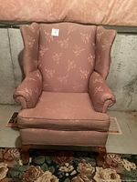 Front view of the dusty rose wingback chair featuring cream floral patterns, rolled arms, and cushioned seat.