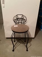 Full front view of the vintage wrought iron vanity stool showing the metal curved and scrollwork backrest design, round upholstery seat, and slender curved iron legs.