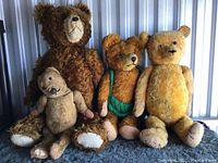 Group photo of four fully jointed vintage teddy bears with varying shades of brown and tan fur, some wearing clothing or accessories.