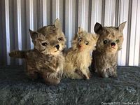 Three vintage plush cats arranged side by side on a dark cloth surface, showing overall condition and size.