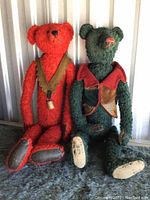 Two vintage teddy bears, one orange and one green, sitting upright on a fabric surface against a metal backdrop.