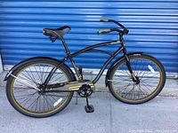 Side view of black Huffy Cranbrook adult bicycle showing overall frame, tires with gold accents, pedals, saddle and curved handlebars.