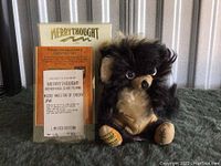 Teddy bear sitting next to its certificate showing limited edition number 65 out of 1000, and box in background.