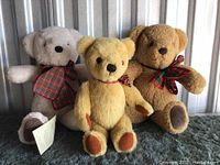 Three plush teddy bears side by side showing variety of colors and plaid bows