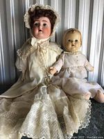 Full shot of two porcelain dolls sitting side by side, showing dresses and facial features.