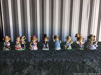 Full set of 10 T. Eaton Punkinhead holiday bear bells displayed in a row on a dark cloth surface with a corrugated metallic background.