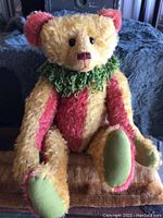 Front view of the mohair teddy bear sitting down, showing color pattern and green fringed collar