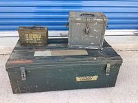 Three metal trunks and ammo boxes stacked in front of a blue metal roll-up door