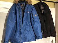 Photo showing two winter jackets hanging, blue one with fur trim and black plain one