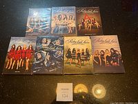 Photo showing all seven DVD cases of Pretty Little Liars seasons arranged on a dark surface with a MaxSold lot number card.