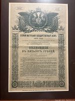 Close-up image of the 1915 Russian bond certificate with Cyrillic text and imperial double-headed eagle emblem, framed in wood.