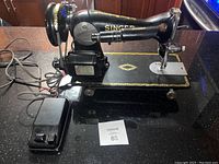 Full side view of the antique Singer sewing machine showing the machine, foot pedal, motor, and electrical cords on a countertop.