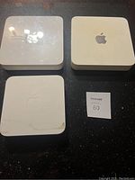 Three white Apple networking devices including two Time Capsules and one AirPort Extreme router on a black surface.
