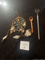 Photo showing a handmade dreamcatcher with natural feathers, a small brown ceramic spoon decorated with white dots, and a metal back scratcher with an extendable handle.