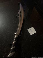 Full length view of curved fantasy sword with blade, handle, and part of case visible on a black surface