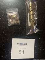 Photo of a gold-tone dragon/claw finger ring and a small resealable bag containing a miscellaneous necklace with gems on a black surface.