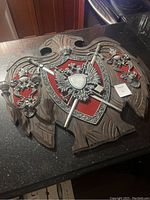Full view of the large wooden carved crest with mounted metal emblem, swords, and candle holders.