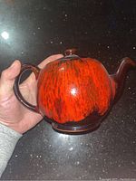 Orangelite Canada pottery teapot with orange and dark brown glaze and handle shown from the side