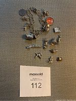 Silver tone charm bracelet laid out with various charms visible including an orange cameo charm, skull, barrel, wrapped candy, and animal-shaped charms.