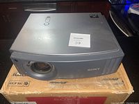 Front and top view of Sony VPL-AW15 projector resting on a cardboard box, showing lens and Sony logo.