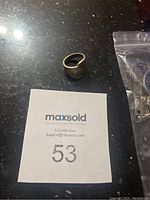 Photo of sterling silver ring shaped from a fork, placed on a dark reflective surface with MaxSold lot number card.