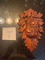 Front angled view of wood carved wall mounted match holder with floral and leaf design details.