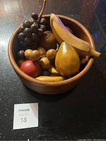 Wooden bowl filled with various handcrafted wooden fruit pieces including grapes, banana, pear, apple, gourd shapes