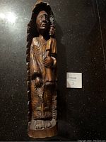 Front view of the large carved wooden statue showing detailed facial features and hands holding a smaller figure.