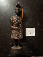 Front view of the dark hardwood hand-carved African woman statue standing on a circular base, patterned dress, with basket on head.