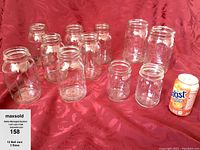 12 Ball brand clear glass jars in three size groups arranged on a red fabric background with a soda can for size reference.