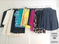 Photo of 11 pieces of women's clothing hanging on a rack including coats, blazers, dresses, and tops.