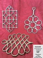 Three different steel trivets arranged on a red textured fabric with a label showing lot number 147. The trivets show varying loop and ring patterns.