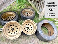 4 gold-colored drag racing rims shown, two rims are mounted with heavily worn tires, set placed on grass beside wooden lattice.