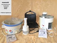 Photo of four kitchen appliances on table: Crock Pot slow cooker, small manual chopper, black waffle iron, and white Breville juice extractor with manuals.